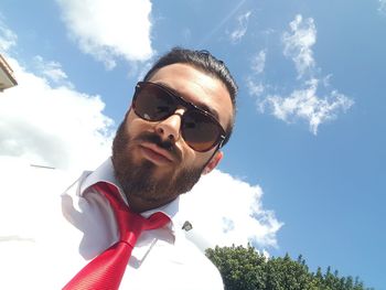 Portrait of young man wearing sunglasses and necktie against sky