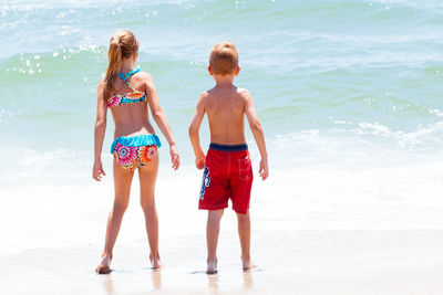 Rear view of siblings standing at beach during sunny day