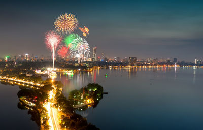 Firework display over illuminated city against sky at night