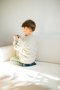 Side view of boy kneeling on bed at home