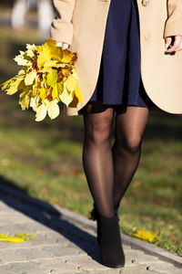 Low section of woman holding leaf walking on street