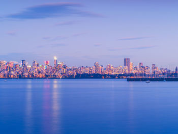 Illuminated buildings by sea against sky at dusk