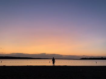 Silhouette people on beach against sky during sunset