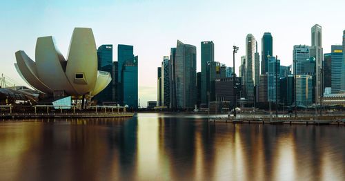 Modern buildings by river against sky in city