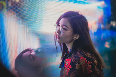 Close-up of young woman standing against illuminated city at night