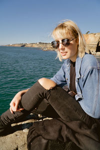 Young woman sitting by sea against sky