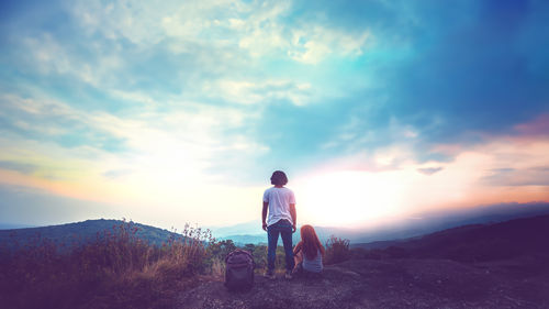 Rear view of man standing on mountain against sky during sunset