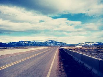 Road leading towards mountains against cloudy sky