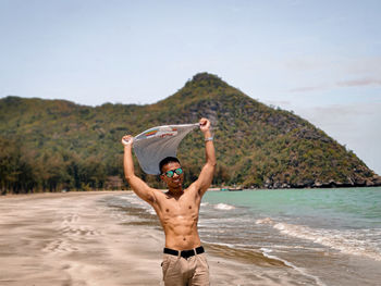 Full length of shirtless man standing at beach against sky