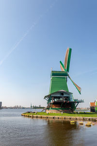 Traditional windmill in lake against clear blue sky