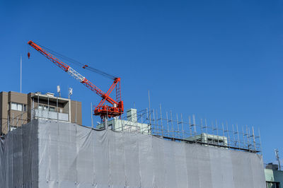 Low angle view of crane at construction site against clear blue sky