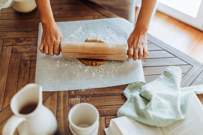 Female hands rolling dough for cookies at the table, top view