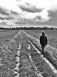 Rear view of man walking on field against cloudy sky