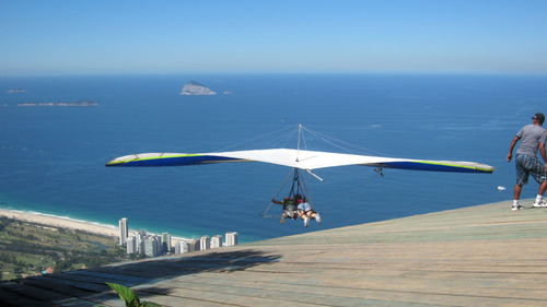 Rear view of people hang-gliding over sea against sky