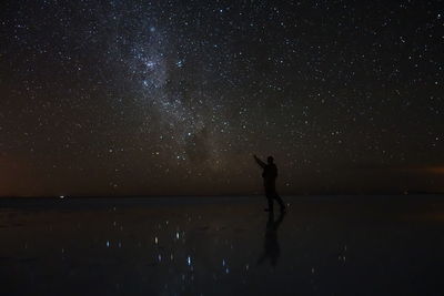 Silhouette person standing on frozen lake against star field at night