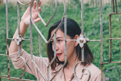 Portrait of young woman holding umbrella by fence