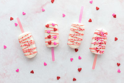 Valentine's day cakesicles with sprinkles on a pink marble surface.