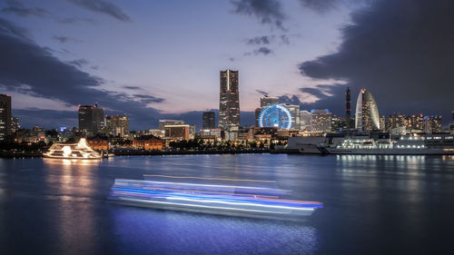 Illuminated buildings by river against sky at night