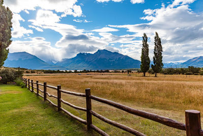 Wooden fence on field by mountains against sky