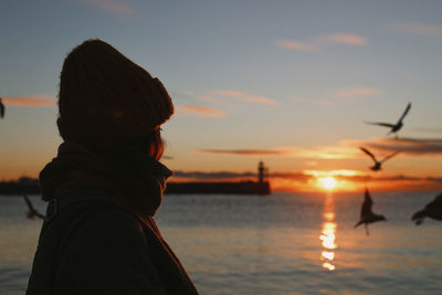 Rear view of silhouette woman standing against sea during sunset