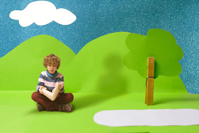 Full length of boy holding book against mountain made with paper in studio