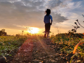 Rear view of woman standing on field against sky during sunset