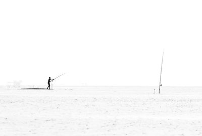 Man fishingon beach against clear sky