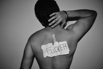 Rear view of shirtless man with sticker against gray background