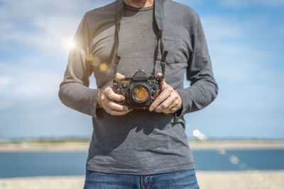 Midsection of man holding camera against sky