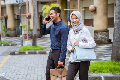 Side view of young woman drinking water while standing in city