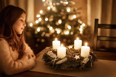 Child sits alone in front of a glowing advent wreath and looks forward to christmas