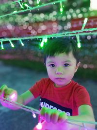 Portrait of boy holding string lights outdoors at night