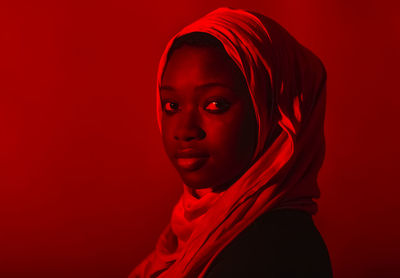 Young woman in hijab staring in front of red background