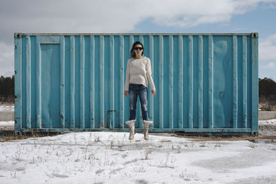 Full length of woman levitating against metallic container during winter