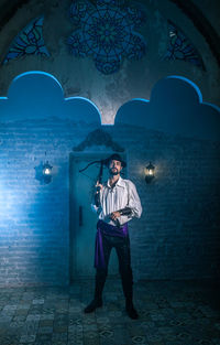 Portrait of man in costume standing against door of abandoned building at night