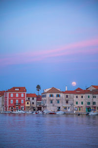 Buildings by sea against sky at dusk