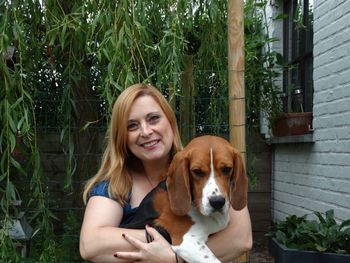 Portrait of smiling young woman carrying beagle against tree at yard