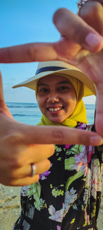 Portrait of smiling young woman wearing hat standing at beach