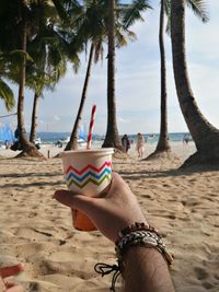 Cropped hand holding drink at beach