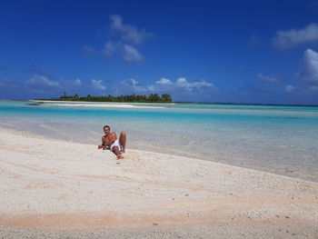 Man sitting at beach against blue sky