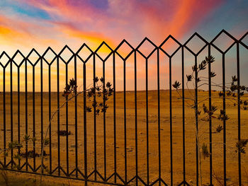 Fence on beach against sky during sunset