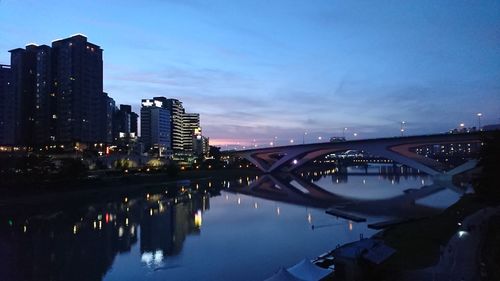 Illuminated bridge over river by buildings against sky in city