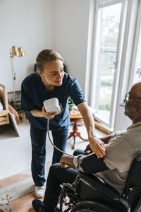 Female doctor doing medical test to elderly male sitting in wheelchair at care home