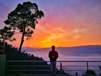 Silhouette man standing by railing against orange sky