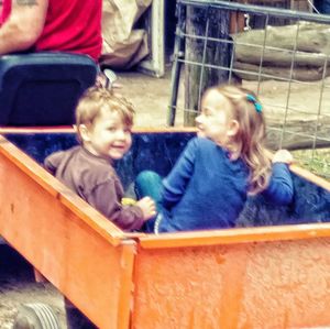 Cute boy and girl looking at camera while sitting on man