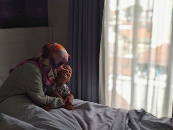 Mother embracing son while sitting on bed at home