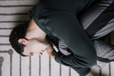 Directly above view of man lying down in fetal position on carpet at home