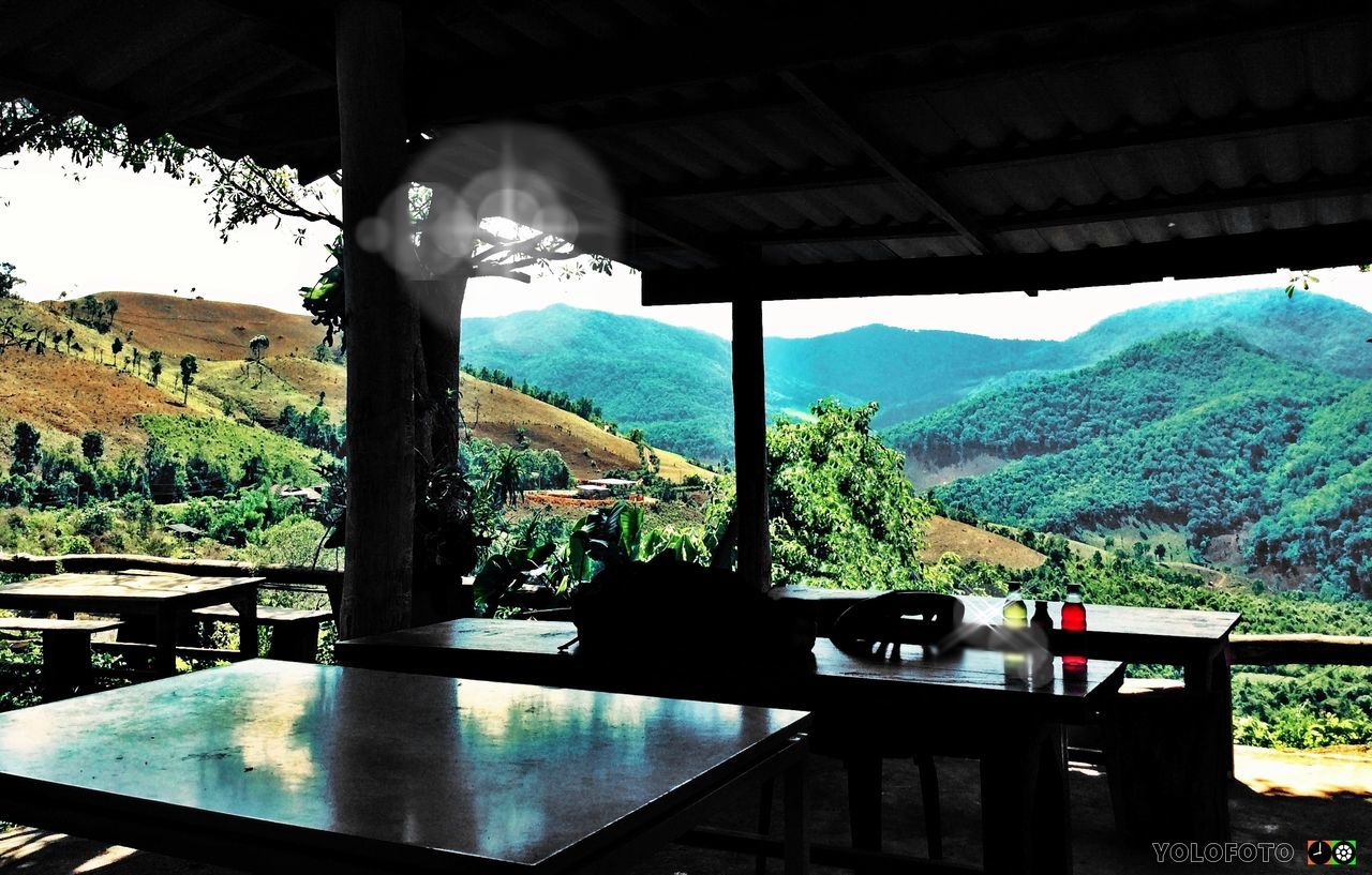 mountain, mountain range, indoors, built structure, window, architecture, sunlight, tree, landscape, railing, blue, nature, clear sky, sky, day, transparent, scenics, tranquility, house, beauty in nature