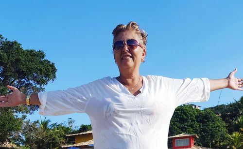 Carefree smiling mature woman with arms outstretched standing against clear sky