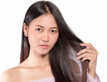 Close-up portrait of beautiful young woman holding hair against white background